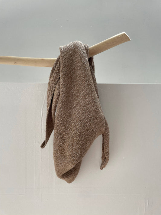 Brown alpaca wool shawl hanging on a wooden rod against a light gray wall.