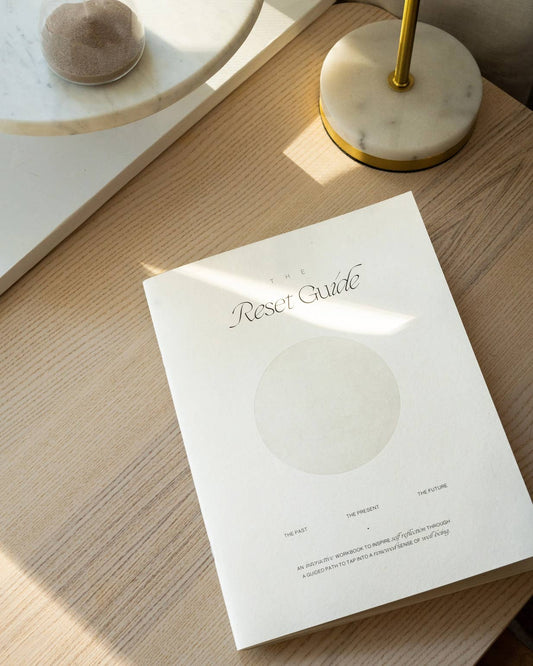 White book titled 'The Reset Guide' on a wooden surface with soft shadows