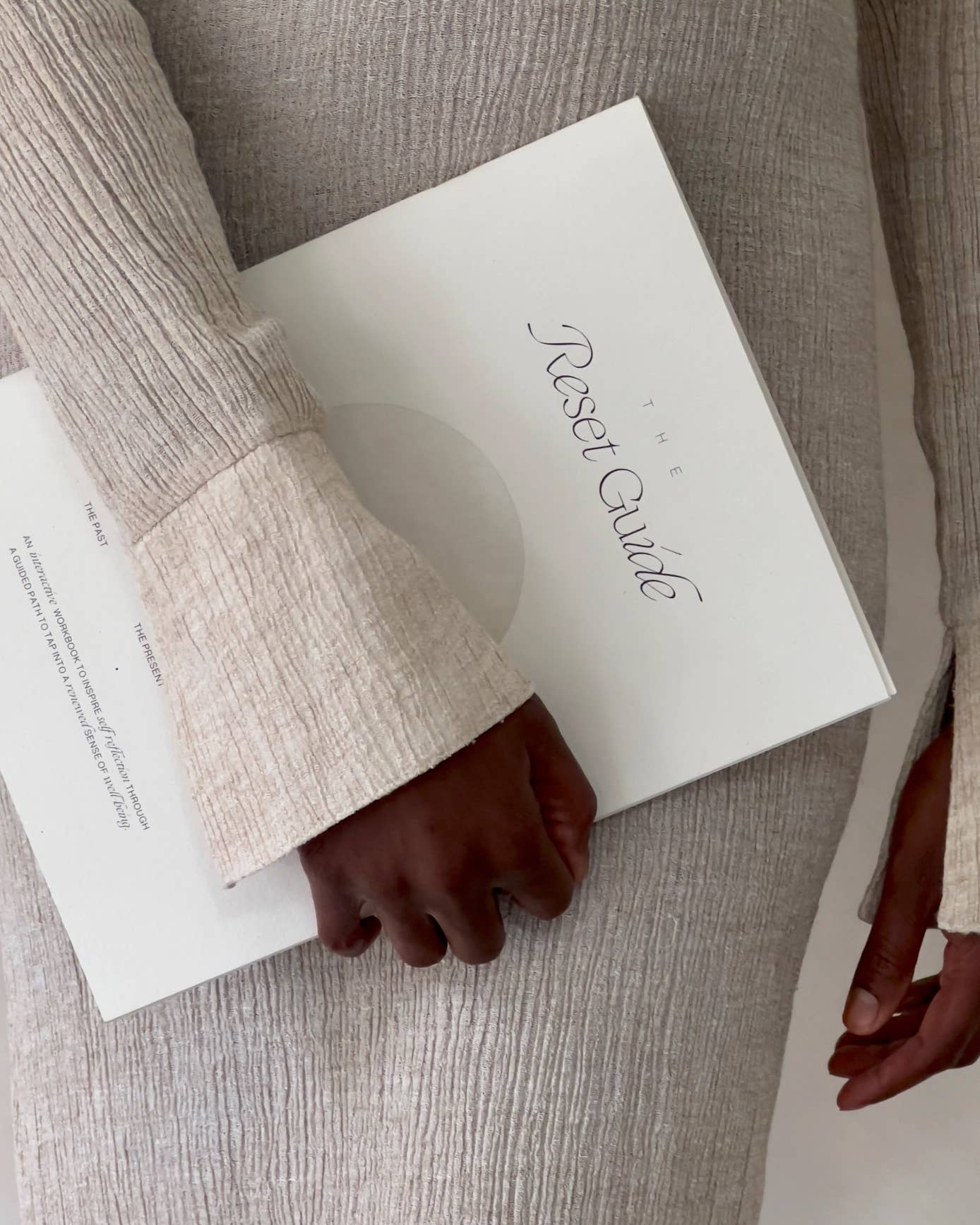 Person holding a journal titled 'The Reset Guide' with a neutral background