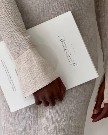 Person holding a journal titled 'The Reset Guide' with a neutral background