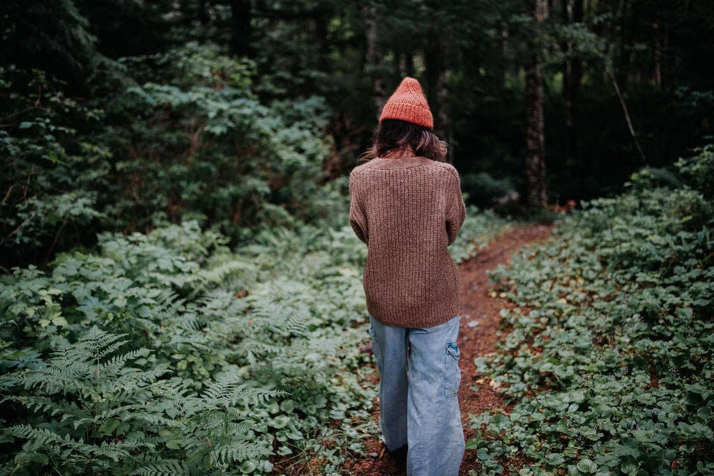 Woman walking away on a forest path wearing a brown wool cardigan.