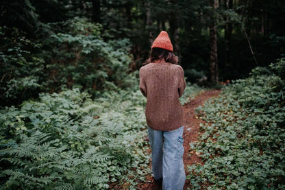 Woman walking away on a forest path wearing a brown wool cardigan.